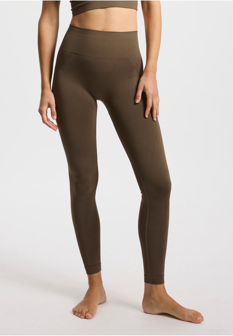 Leggings marron taille haute en tissu extensible, dotés d'un design sans coutures et d'une silhouette ajustée, avec des coutures minimales et sans poches.