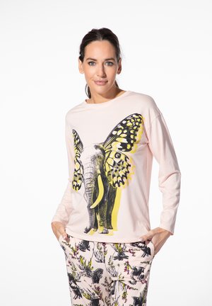Woman wearing light pink top with an elephant and butterfly wings graphic and matching pants with black animal and floral patterns.