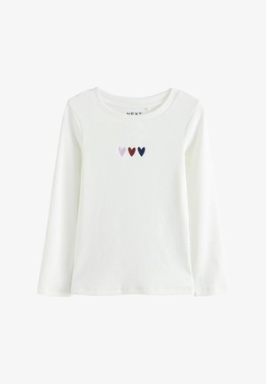 Vit långärmad topp med ribbad textur, rund halsringning och tre små broderade hjärtan i rosa, vinröd och marinblå.
