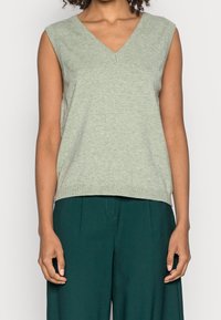 Haut sans manches vert clair avec un col en V. Confectionné dans un tissu doux, il présente une coupe décontractée et un ourlet côtelé, accompagné d'un pantalon vert foncé.