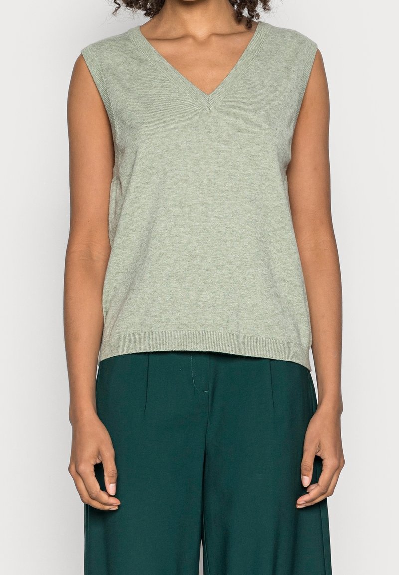 Haut sans manches vert clair avec un col en V. Confectionné dans un tissu doux, il présente une coupe décontractée et un ourlet côtelé, accompagné d'un pantalon vert foncé.