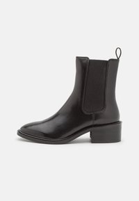 Botín de cuero negro hasta el tobillo con paneles laterales elásticos, punta redonda y tacón bajo. Presenta costuras decorativas y una lengüeta en la parte trasera.