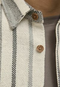 Vævet skjorte i lys beige og grå vertikale striber. Har en struktureret krave og en træknap med et lille design.