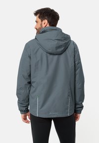 Giacca impermeabile grigia con cappuccio, polsini elasticizzati e dettagli riflettenti. Caratterizzata da una texture liscia e sleek e un design dalla vestibilità rilassata.