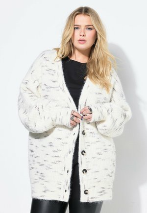 Cardigan blanco esponjoso con textura de canalé, que presenta un corte relajado, grandes botones y sutiles motas grises. Mangas largas con detalles en los puños.