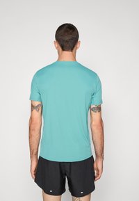 Turquoise athletic t-shirt with short sleeves, smooth texture, and crew neck. Worn with black shorts, featuring visible tattoos on arms.