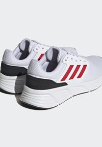Baskets de sport blanches avec un dessus en maille respirante, des accents rouges et un soutien au talon noir. Semelle épaisse et rembourrée pour le confort.