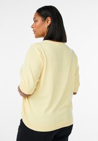 Kurzärmeliger gelber Strickpullover mit gerippten Bündchen und Saum, mit lockerem Schnitt und glatter Textur. Rückansicht gezeigt.