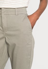 Světlé šedé, zúžené kalhoty vyrobené ze směsové bavlny; obsahují přední kapsy a viditelné švy. Hladká textura s ležérním designem.