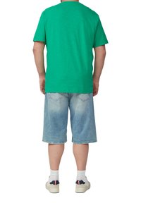 Zielona bawełniana koszulka w luźnym fasonie, zestawiona z jasnoniebieskimi szortami dżinsowymi o wyblakłym odcieniu i dwóch tylne kieszenie, noszona z białymi skarpetkami i tenisówkami.