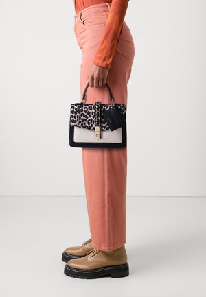 Borsa a mano in stampa leopardata con base liscia color crema, dettagli neri e un lucchetto dorato. Stivali marroni con lacci e pantaloni rosa completano il look.