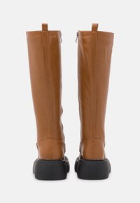 Bottes montantes en cuir marron avec une texture lisse, bout rond, semelle en caoutchouc noire et fermeture éclair à l'arrière.
