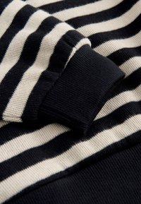 Gros plan d’un tissu tricoté à rayures horizontales noires et blanches avec un bord-côte noir replié sur les rayures.