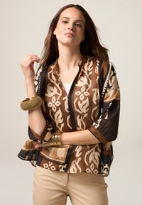 Braun gemusterte Bluse mit kurzen Ärmeln, die florale und abstrakte Designs zeigt. Der Stoff hat eine glatte Textur; kragenloser Ausschnitt.