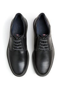 Scarpe in pelle nera con una texture liscia, design con lacci e cuciture grigie a contrasto. L'interno presenta una fodera blu scuro.