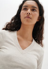 Beige geripptes Langarmshirt mit V-Ausschnitt, feiner Textur, subtilen Nähdetails und taillierter Passform.