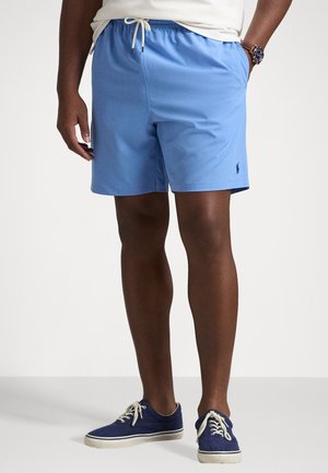 Costumi da bagno blu chiaro con vita elastica e cordoncino. Presentano un piccolo logo sulla coscia sinistra. Indossati con sneaker blu.
