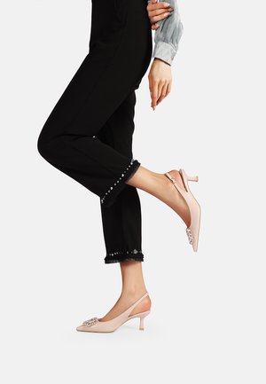 Slingback con tacco a punta di un delicato rosa chiaro, con decorazioni traslucide e tacco sottile, abbinati a pantaloni neri a 3/4 con dettagli decorativi.