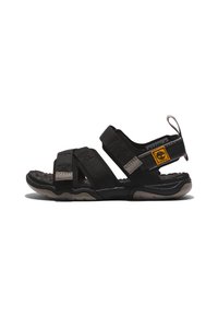Sandal preto com correias ajustáveis feitas de tecido texturizado, apresentando uma palmilha acolchoada e sola de borracha durável. Acento do logótipo amarelo.