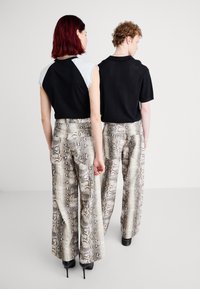 Due persone che indossano top contrastanti: uno nero a maniche corte e l'altro azzurro chiaro. Entrambi hanno pantaloni larghi a stampa serpente.