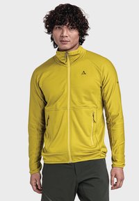 Gelbe Zip-Jacke mit gerippter Textur, zwei Fronttaschen und hohem Kragen. Mit einem Logo auf der Brust und kontrastierenden Reißverschlüssen.