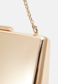 Złota metaliczna kopertówka o gładkiej powierzchni, wyposażona w łańcuszkowy pasek i zapięcie zatrzaskowe u góry.
