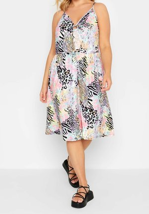 Kobieta nosząca sukienkę bez rękawów, do kolan, z wielokolorowym pastelowym zwierzęcym wzorem oraz czarne sandały na platformie z paskami.