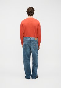 Κόκκινο πουκάμισο με μακριά μανίκια, συνδυασμένο με μπλε τζιν παντελόνι. Το πουκάμισο έχει στρογγυλή λαιμόκοψη, ενώ το τζιν είναι με ίσια γραμμή και εμφανείς πίσω τσέπες.