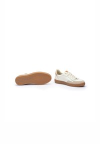 Un par de zapatillas bajas blancas y beiges con suelas de goma marrón, una zapatilla en posición vertical y la otra mostrando la suela con el logo "Pikolinos".