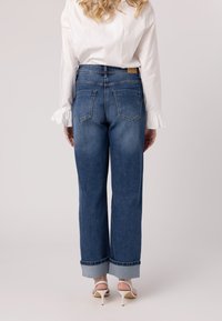 Jeans in denim blu ad alta vita e gamba ampia, con una finitura sbiadita, orli arrotolati e due tasche posteriori. Abbinati a una maglietta bianca a maniche lunghe.