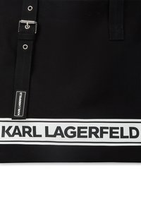 Fekete szövet bevásárlótáska állítható pánttal, ezüst csattal és fehér sávval, amelyen vastag "KARL LAGERFELD" felirat található.