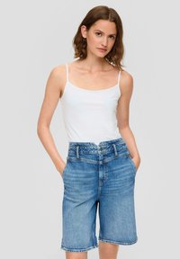 Hellblaue Denim-Shorts mit hoher Taille und fünf Taschen. Glatte Textur und umgeschlagener Saum. Kombiniert mit einem eng anliegenden weißen Tanktop.