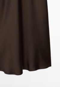 Hnědá saténová sukně s hladkou strukturou, splývavým designem a vlnkovaným lemem. Tkanina se zdá být lehká a elegantně splývá.