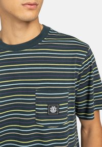 Short-sleeve cotton t-shirt featuring navy background with multicolored horizontal stripes, a chest pocket, and a logo patch on the pocket.