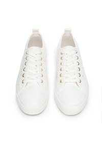 Weiße Schnürsneaker mit strukturierten Seiten, flachen Schnürsenkeln und goldfarbenen Ösen. Gummisohle mit gemustertem Dekor. Leichtes Stoffmaterial.
