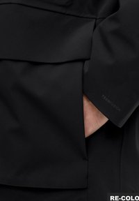 Čierna bunda s hladkou, matnou textúrou látky. Výrazným detailom je logo "TECHFUSION" vytlačené na manžete.