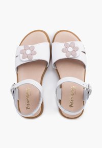 White sandals with two straps, floral fabric accents, adjustable ankle buckle, and a textured sole. Minimalist design with a cushioned footbed.