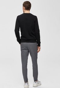 Camicia nera a maniche lunghe con polsini a coste, abbinata a pantaloni grigi a gamba affusolata. L'outfit presenta una vestibilità casual e una texture morbida.