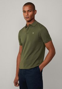 Olive zelené polo tričko s krátkymi rukávmi, s klasickým golierom a malým zlatým logom na hrudi, vyrobené z hladkej tkaniny.