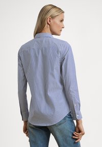 Blå og hvitstripet skjorte med lange ermer, knapp mansjetter og klassisk krage. Baksiden har et skulderstykke og buet kant.