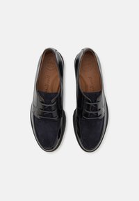 Scarpe in pelle nera con finitura liscia, dotate di una parte anteriore in camoscio, chiusura con lacci e solette marroni contrassegnate "SUPER SOFT".
