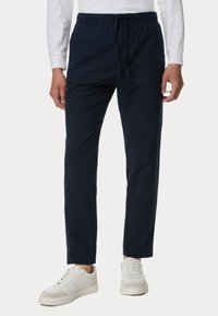 Pantaloni da jogging in blu navy, tessuto intrecciato con vita elastica e cordino. Tessuto testurizzato, aderenti alla caviglia. Abbinati a sneakers bianche.