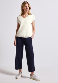 Cremefarvet, struktureret V-hals top parret med navy brede bukser og hvide sneakers, der har en afslappet pasform og uformel stil.
