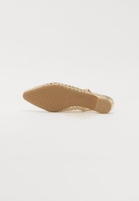 Chaussure plate en paillettes dorées avec un bout pointu, de fines lanières et une semelle en caoutchouc texturée. La semelle intérieure présente une empreinte de logo.