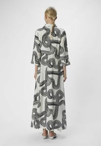 Robe maxi en tissu blanc avec des motifs en vagues abstraites noires. Dispose de manches trois quarts et d'une coupe ample, avec un ourlet droit.