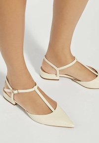 Beige slingback flats met een spitse neus en een gestructureerde afwerking. Voorzien van dunne bandjes en een kleine enkelgesp voor een veilige pasvorm. Platte hak.