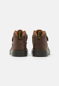 Botas dchelas marrones con un upper de cuero texturizado, forro naranja, costuras amarillas y una suela de goma negra con un patrón de agarre.