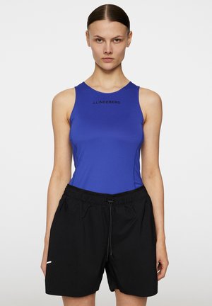 Koninklijk blauwe mouwloze top met subtiele logo; gecombineerd met losse zwarte shorts met elastische tailleband en koord. Gladde textuur.