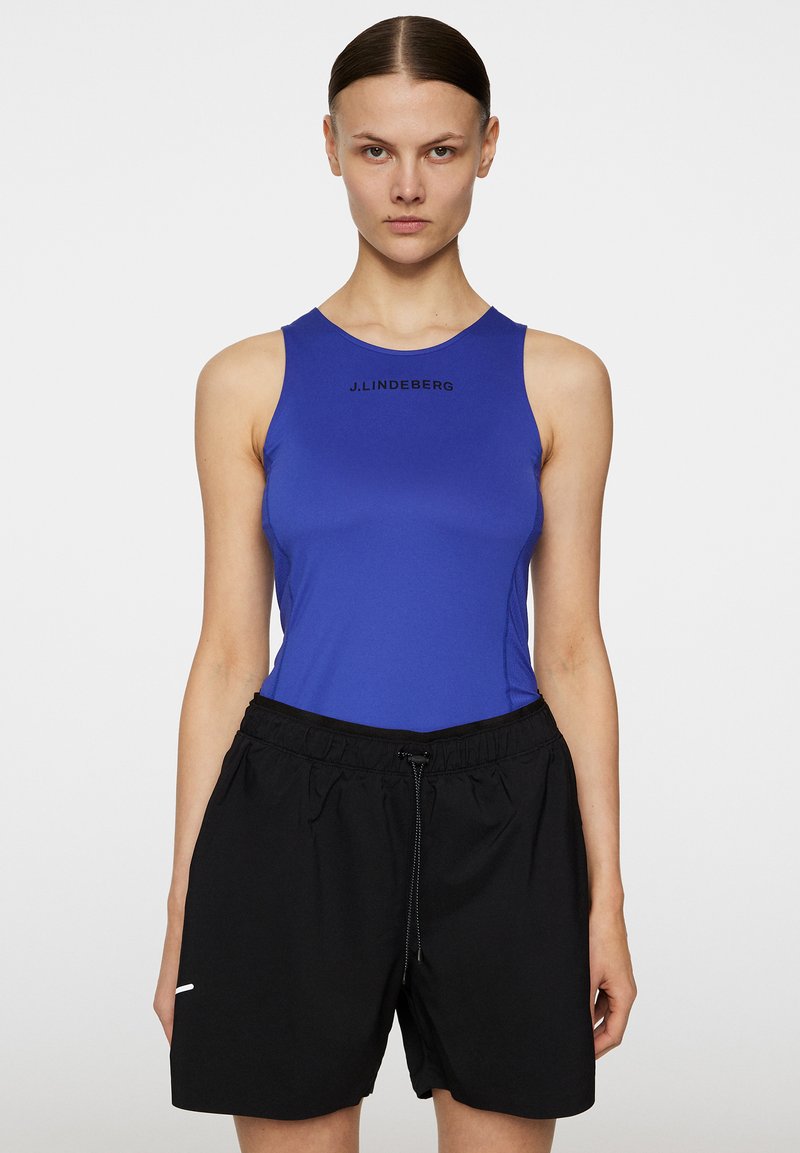 Kungablå ärmlös topp med diskret logotyp; matchad med lösa svarta shorts med elastisk midja och dragsko. Slät textur.