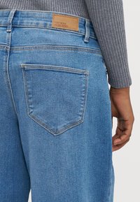 Svetlo modre jeans hlače iz denima z gladko teksturo, z zadnjim žepom, rjavim logotipom na pasu in ravno krojem.